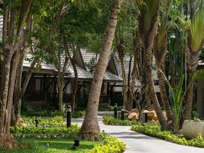 Weg zwischen Palmen zu einer Hotelanlage mit moderner Architektur und grüner Umgebung.