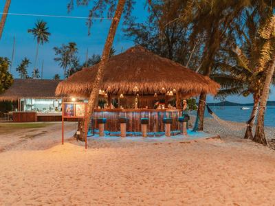 Strandbar mit Strohdach und Sitzgelegenheiten bei Sonnenuntergang am Meer.