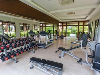 Moderner Fitnessraum mit Hanteln, Laufbändern und anderen Trainingsgeräten, große Fenster mit Gartenblick.