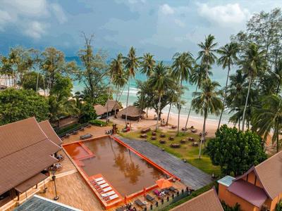 Blick auf einen Pool neben Palmen und einem Sandstrand mit Stühlen und Hängematten.