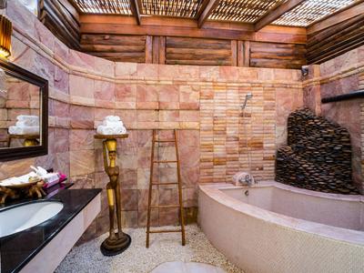 Rustic bathroom with natural stone walls, a large bathtub, and wooden details.