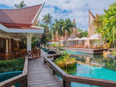 A tropical resort with wooden walkways, pool, and traditional Thai roofs under a blue sky.