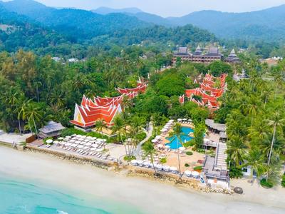 Beach resort with pool, sun umbrellas, and tropical greenery by forested hills.