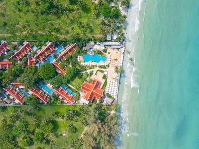 Aerial view of a resort with red roofs, pool, and adjacent beach