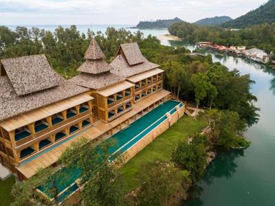 Hotel with traditional architecture beside river and lush greenery in a tropical setting.