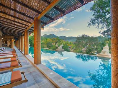 An infinity pool overlooking mountains and sky, surrounded by lounge chairs under a covered area.