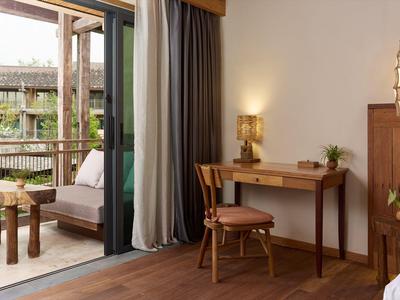 Helles Hotelzimmer mit Schreibtisch, Stuhl und Terrasse mit Sitzbereich.