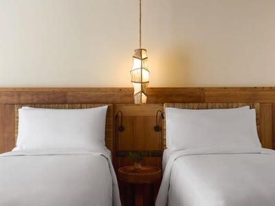 Zwei Einzelbetten mit weißen Bettwäsche und Holzkopfteil, mittig ein Nachttisch und hängende Lampe.