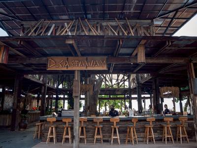 Rustikale Bar mit Holzstühlen und Deckendach in einem offenen, luftigen Raum.