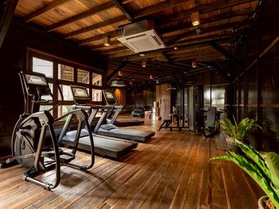 Modernes Fitnessstudio mit Holzfußboden und verschiedenen Trainingsgeräten in warmem Licht.