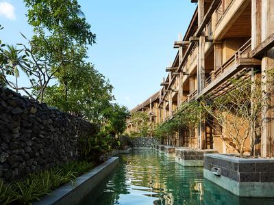 Langer Wasserkanal mit klarem Wasser neben einem Gebäude mit Holzfassade und grünen Bäumen.