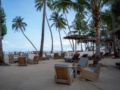 Strandhotel mit Holzstühlen unter Palmen und Blick aufs Meer bei klarem Himmel.