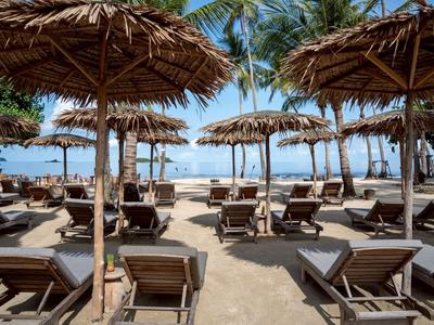 Strand mit Liegestühlen und Palmen, Sonnenschirme aus Stroh, blauer Himmel im Hintergrund