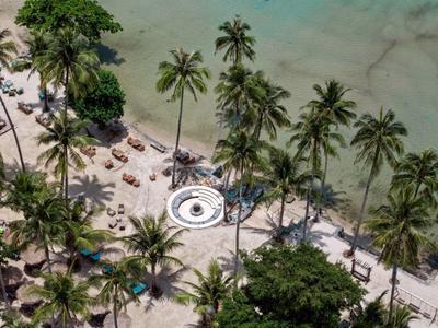 Strand mit Palmen, Sonnenliegen und einem runden Pavillon am Ufer mit klarem Wasser.
