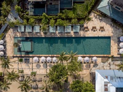 Vogelperspektive auf einen rechteckigen Pool mit Liegestühlen und Sonnenschirmen in einer Hotelanlage.