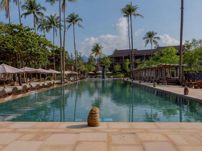 Una gran piscina con tumbonas y palmeras en un resort hotelero bajo un cielo azul.