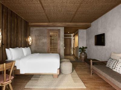 Modernes Hotelzimmer mit großem Bett, Sofa, Holzverkleidung und minimalistischem Design