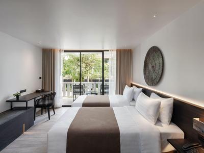 Modernes Hotelzimmer mit großen Betten, Balkon und Blick auf grüne Bäume