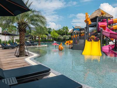 Wasserpark mit bunten Rutschen neben einem Pool und Sonnenliegen mit Palmen.