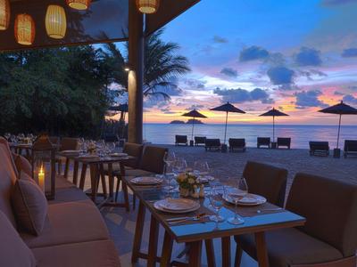 Gemütliche Terrasse eines Restaurants am Strand bei Sonnenuntergang mit Tischen und Stühlen.