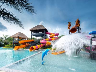 Wasserpark mit Rutschen, Wasserspielen und Palmen unter blauem Himmel.