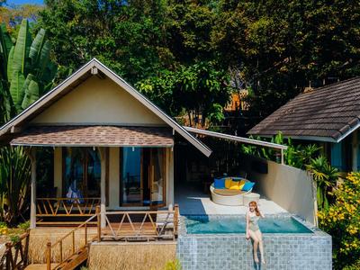 Zwei Bungalows mit Holzterrassen und einem kleinen Pool, umgeben von dichtem Grün.