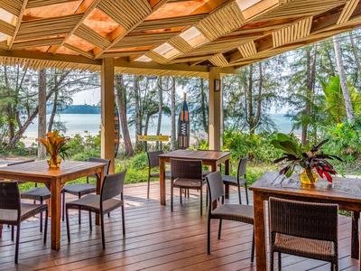 Offener Hotel-Pavillon mit Holzboden und -decke, Tischen, Stühlen und Blick auf Wald und See.