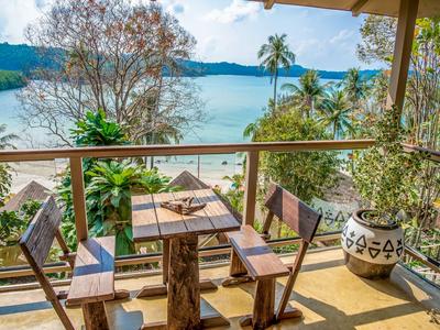 Balkon mit Holztisch und Stühlen mit Blick auf tropische Pflanzen und einen See.