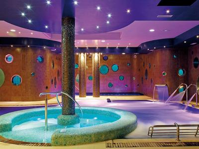 Area spa moderna con idromassaggio illuminato e decorazioni murali rotonde colorate.