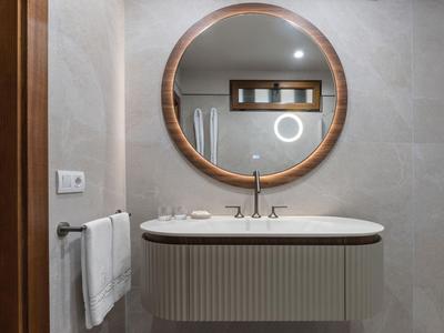 Lavabo moderno de hotel con espejo redondo y paredes grises.
