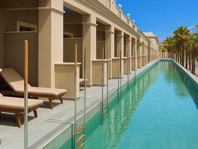 Piscina exterior larga junto a la terraza del hotel con tumbonas y palmeras bajo un cielo azul claro.