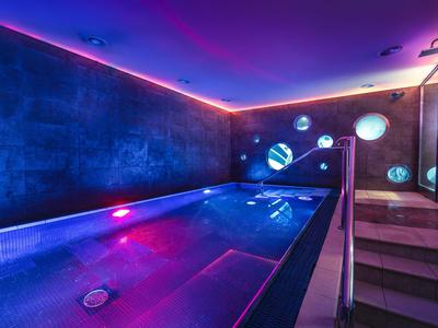 Piscine intérieure moderne avec éclairage LED et luminaires circulaires dans un cadre hôtelier de luxe.