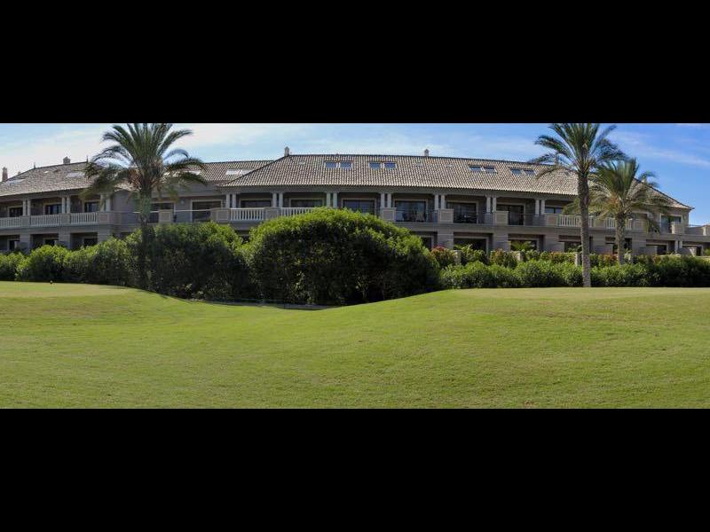 Grande complesso alberghiero con prato curato e palme sotto un cielo azzurro limpido.