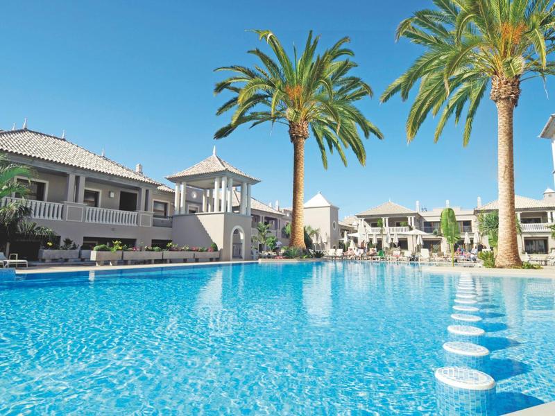 Grande piscina con acqua azzurra limpida, circondata da palme e edifici dell'hotel sotto un cielo sereno.