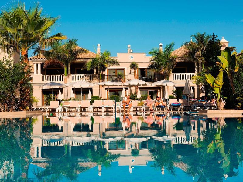 Hotel di lusso con terrazza in vetro e grande piscina circondata da palme.