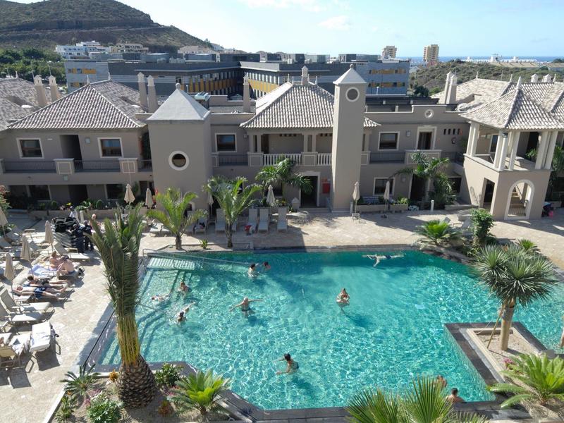 Grande piscina all'aperto con lettini e edificio dell'hotel sullo sfondo, circondato da colline.