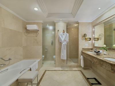 Helles modernes Badezimmer mit Dusche, Badewanne, Waschtisch aus Marmor und weißem Bademantel.