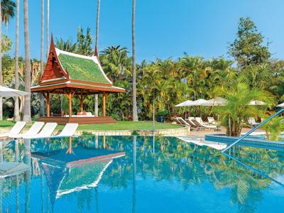 Großer blauer Pool, umgeben von Liegestühlen, grünen Bäumen und einem asiatischen Pavillon.