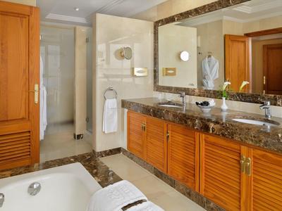Helles Badezimmer mit Holzschränken, großem Spiegel, Marmorarbeitsplatte und Badewanne.