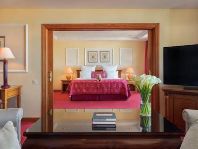 Wohnzimmer mit Sofa, Vase und TV, dahinter Schlafzimmer mit rotem Bett und Bildern an der Wand.