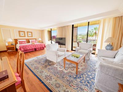 Hell eingerichtetes Hotelzimmer mit Sitzecke, Teppich und großem Balkon mit Meerblick.