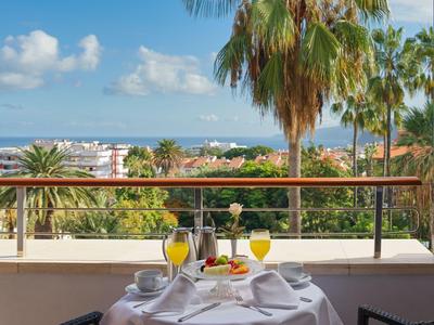 Ein gedeckter Tisch mit Getränken auf einem Balkon mit Blick auf Palmen und das Meer.