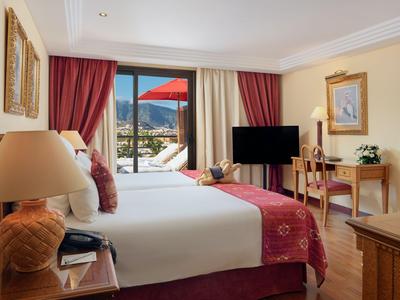 Helles Hotelzimmer mit Doppelbett, Fernseher, Schreibtisch und Balkon mit Bergblick.