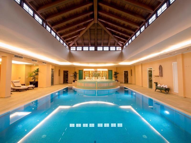 Piscina interna con travi in legno e lettini in un'area spa di lusso.