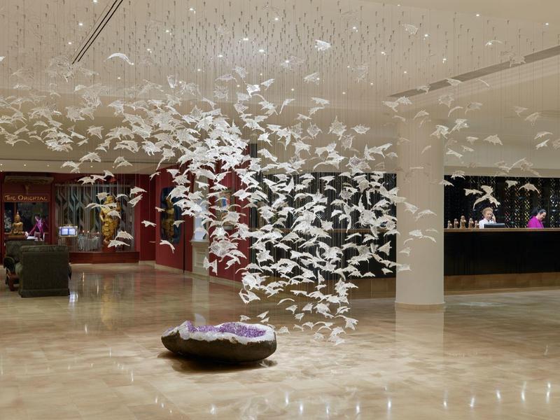 Ampia hall dell'hotel con installazione artistica moderna di uccelli al centro e reception sullo sfondo.