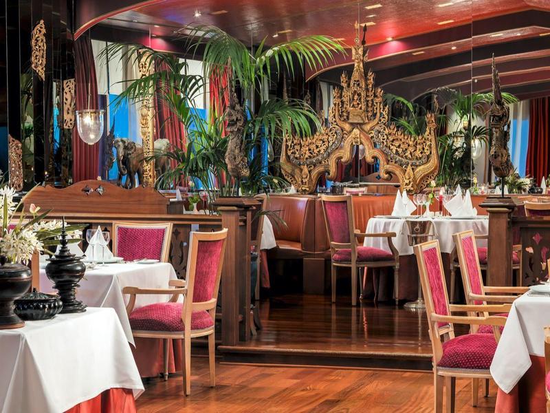 Ristorante elegante con sedie decorative, tovaglie bianche e piante esotiche.