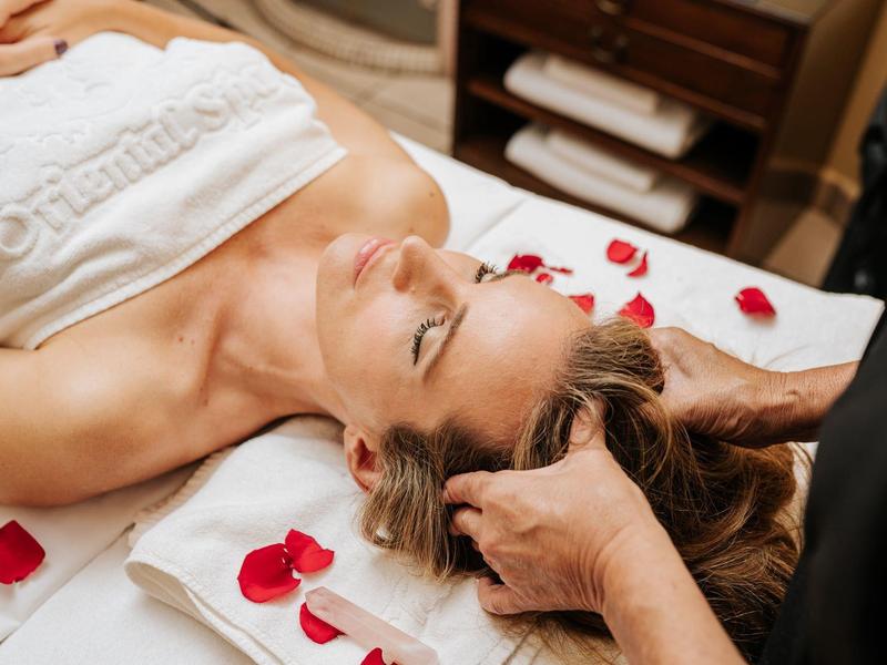 Donna si rilassa con un massaggio alla testa su un lettino spa con petali di rosa.