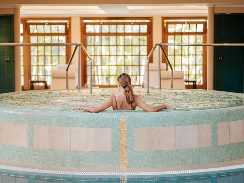 Donna si rilassa in una vasca idromassaggio rotonda con grandi finestre sullo sfondo.