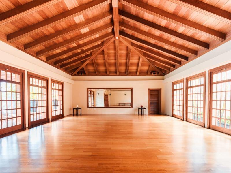 Ampia stanza luminosa con pavimento e soffitto in legno, circondata da finestre con griglie.