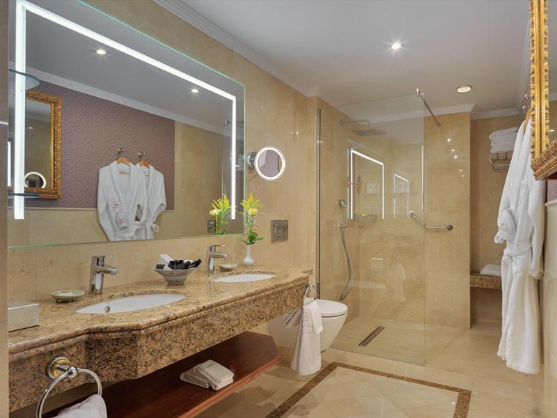Bagno d'hotel moderno con doppio lavabo, grande specchio illuminato e doccia a filo pavimento.